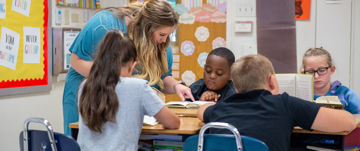 Teacher assisting four students as they read at their desks in class